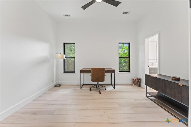 home office with a towering ceiling, light hardwood / wood-style flooring, and ceiling fan