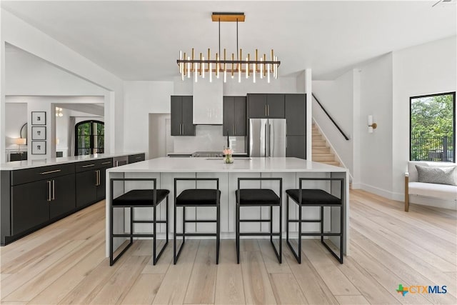 kitchen with stainless steel fridge, a breakfast bar, hanging light fixtures, and light hardwood / wood-style floors