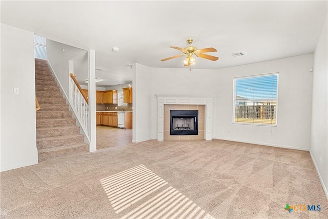 unfurnished living room featuring ceiling fan, light colored carpet, and a tiled fireplace