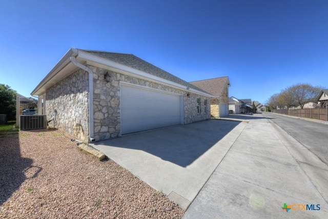 view of home's exterior featuring concrete driveway, central air condition unit, an attached garage, and stone siding