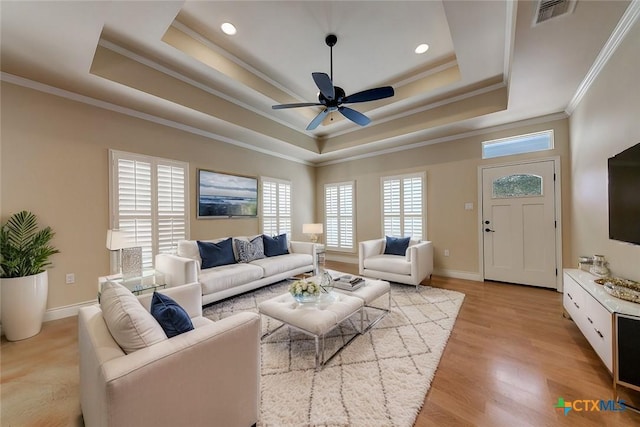 living room featuring visible vents, crown molding, baseboards, a tray ceiling, and light wood-style flooring