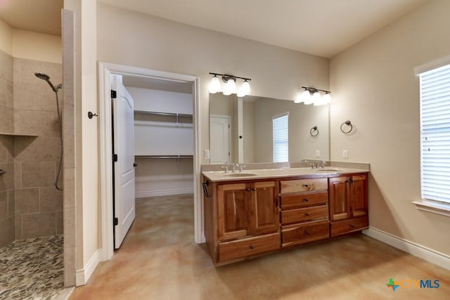 full bathroom featuring a tile shower, double vanity, baseboards, and a sink