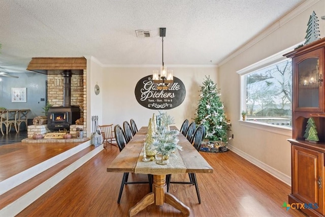 dining room with a wood stove, crown molding, a textured ceiling, and hardwood / wood-style flooring