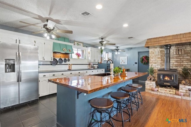 kitchen with a wood stove, sink, stainless steel refrigerator with ice dispenser, a textured ceiling, and white cabinetry