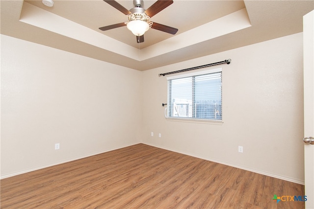 empty room featuring hardwood / wood-style floors, ceiling fan, and a raised ceiling