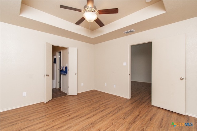 spare room featuring ceiling fan, light wood-type flooring, and a tray ceiling