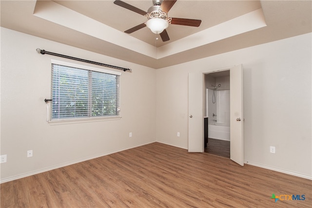 empty room featuring hardwood / wood-style flooring, ceiling fan, and a raised ceiling