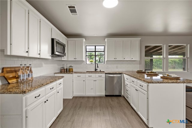 kitchen with a peninsula, stone countertops, stainless steel appliances, and visible vents