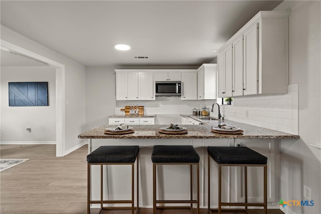 kitchen featuring a peninsula, stone countertops, white cabinetry, stainless steel microwave, and baseboards