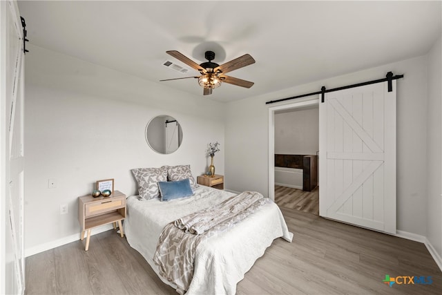 bedroom with baseboards, visible vents, a barn door, and wood finished floors