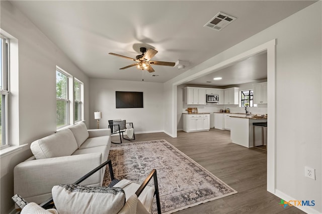 living area featuring baseboards, a healthy amount of sunlight, visible vents, and a ceiling fan