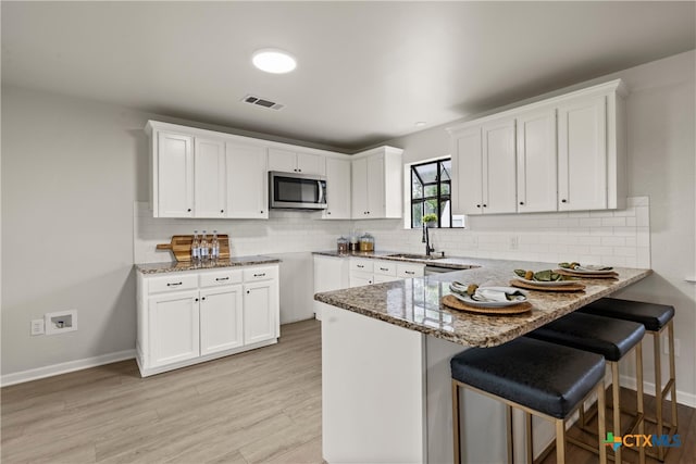 kitchen with a peninsula, a sink, stone countertops, visible vents, and stainless steel microwave