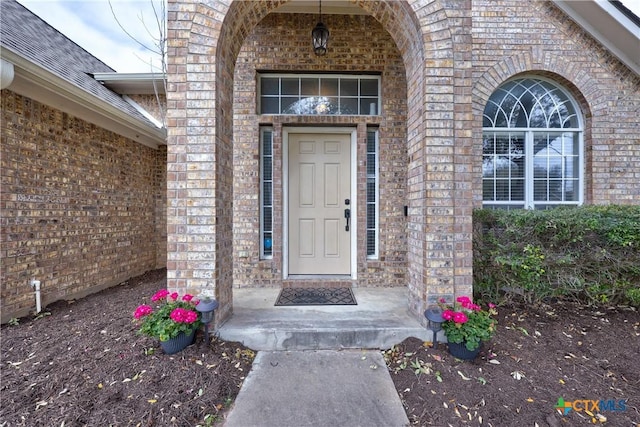 property entrance featuring brick siding and a shingled roof