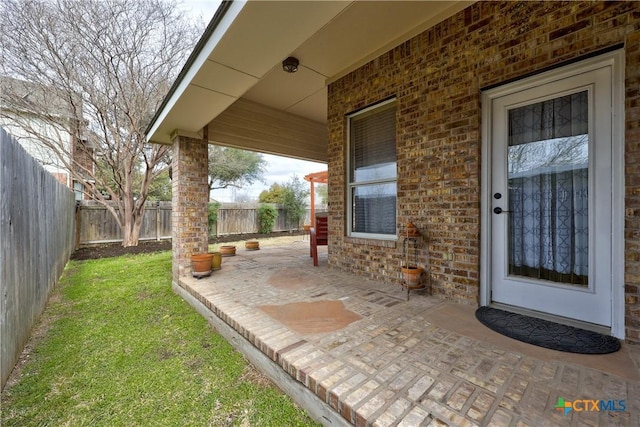 property entrance featuring a patio area, fence, brick siding, and a lawn