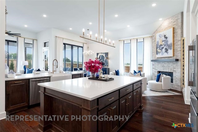 kitchen featuring open floor plan, dishwasher, light countertops, a fireplace, and dark wood-style flooring