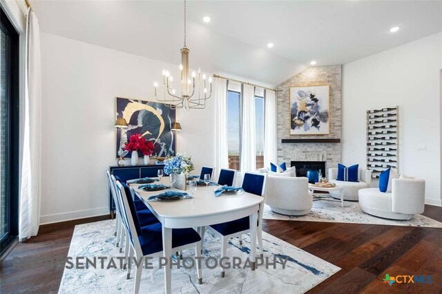 dining area with wood finished floors, an inviting chandelier, a fireplace, baseboards, and vaulted ceiling