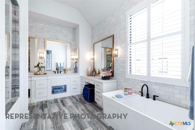 full bathroom with vanity, tile walls, a soaking tub, and lofted ceiling