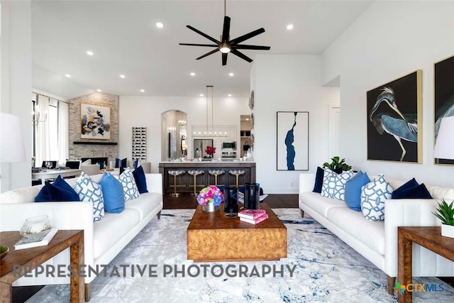 living area with arched walkways, a fireplace, ceiling fan, and wood finished floors