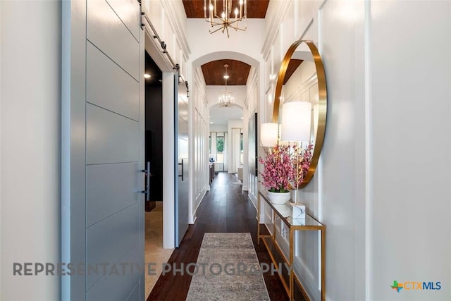 corridor featuring an inviting chandelier, dark wood-type flooring, and a barn door