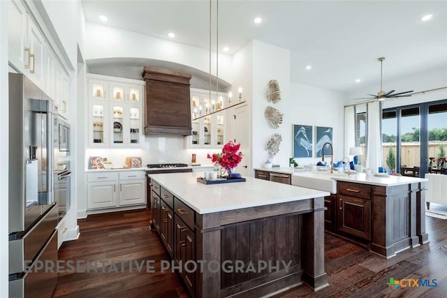 kitchen featuring dark brown cabinets, a center island, white cabinets, stainless steel appliances, and a sink