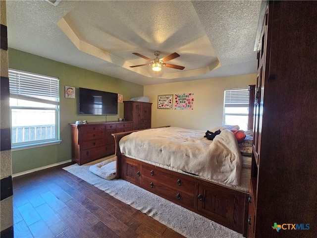 bedroom featuring dark wood finished floors, a textured ceiling, a raised ceiling, and baseboards