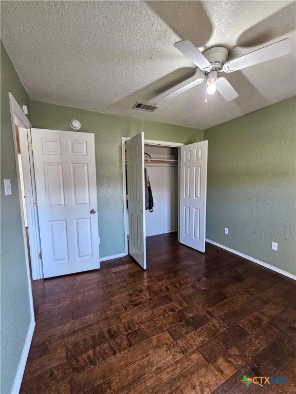 unfurnished bedroom featuring a closet, a ceiling fan, visible vents, baseboards, and a textured ceiling
