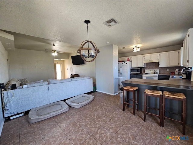 kitchen featuring white cabinetry, a sink, visible vents, open floor plan, and white appliances
