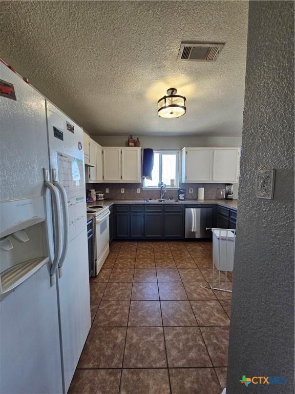 kitchen with white appliances, a sink, white cabinetry, visible vents, and a textured ceiling