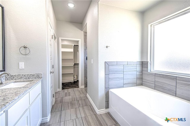 bathroom featuring baseboards, a textured wall, a walk in closet, vanity, and a bath