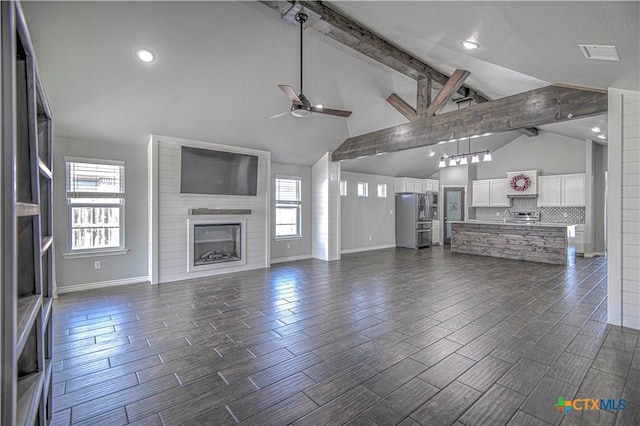 unfurnished living room featuring a large fireplace, wood finish floors, a ceiling fan, baseboards, and beam ceiling