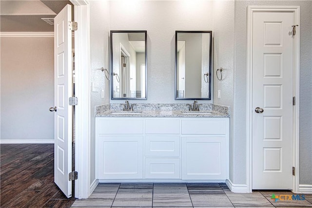 bathroom with double vanity, baseboards, a sink, and wood finish floors