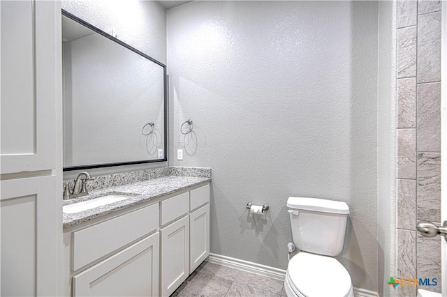 bathroom with a textured wall, vanity, and toilet