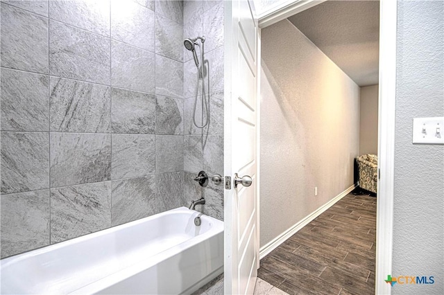 bathroom featuring wood tiled floor, shower / bath combination, a textured wall, and baseboards