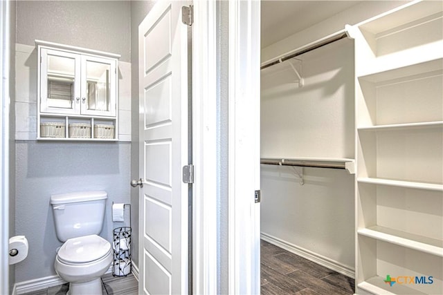 bathroom with baseboards, a walk in closet, toilet, and wood tiled floor