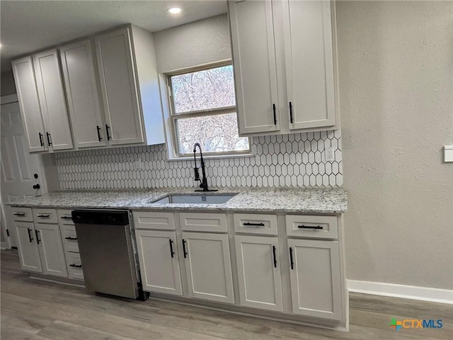 kitchen with light stone counters, stainless steel dishwasher, sink, and tasteful backsplash