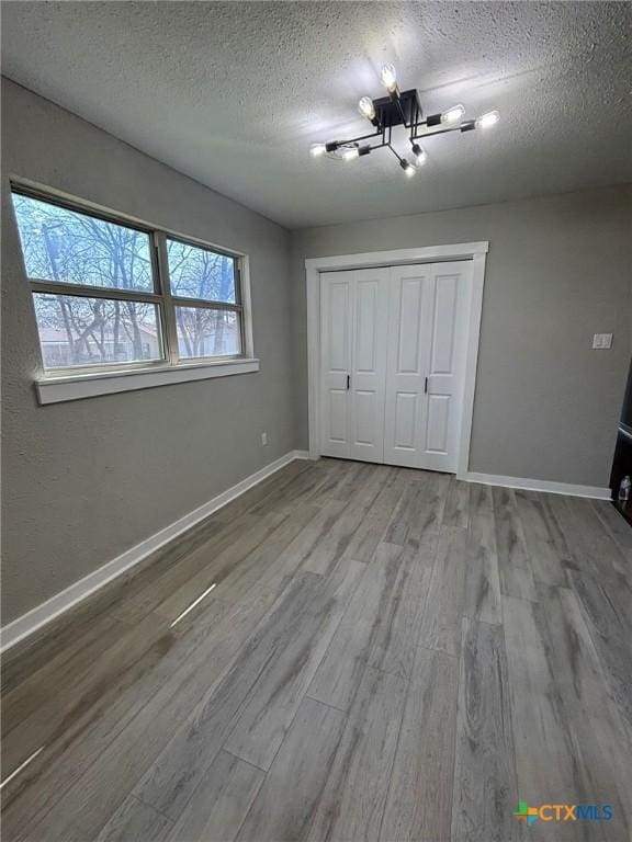 unfurnished bedroom featuring an inviting chandelier, hardwood / wood-style flooring, a closet, and a textured ceiling