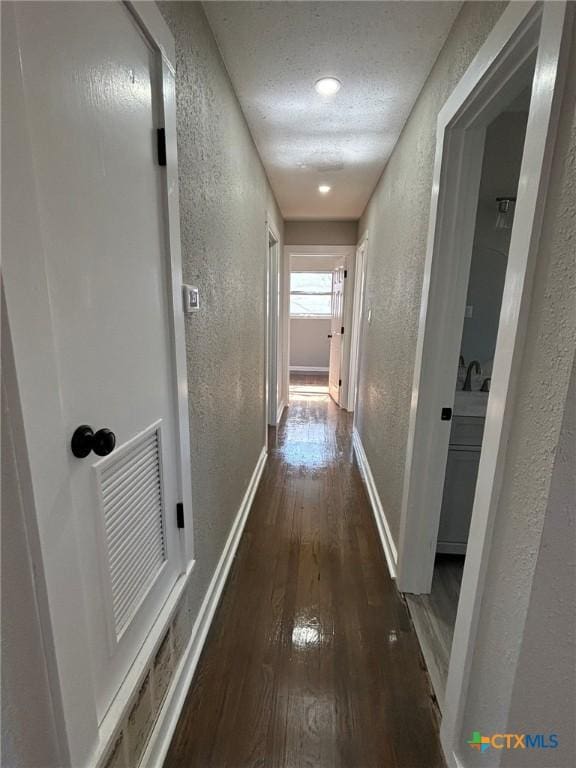 corridor with a textured ceiling and dark hardwood / wood-style flooring