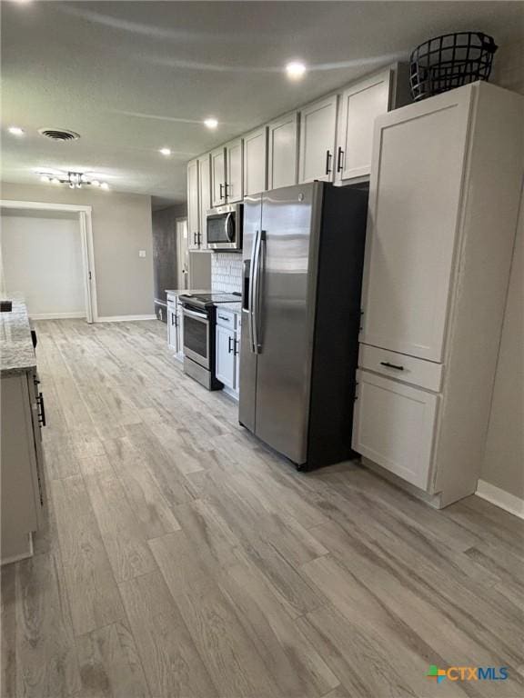 kitchen with white cabinetry, light wood-type flooring, appliances with stainless steel finishes, light stone countertops, and decorative backsplash