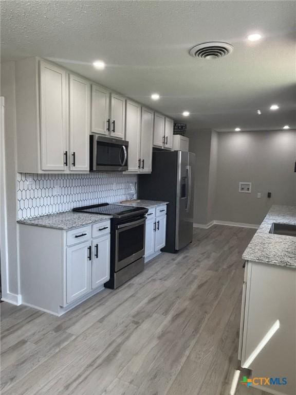 kitchen featuring appliances with stainless steel finishes, white cabinetry, backsplash, light stone countertops, and light wood-type flooring