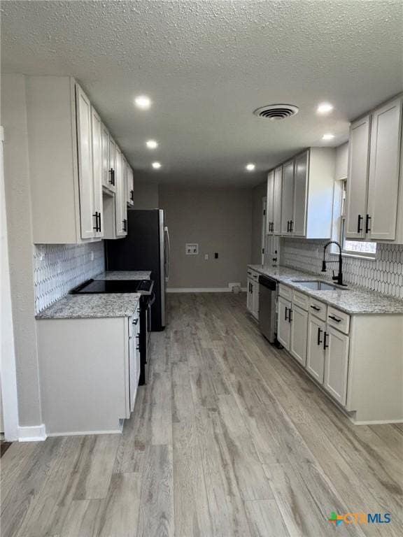 kitchen with sink, dishwasher, light stone counters, light hardwood / wood-style floors, and white cabinets