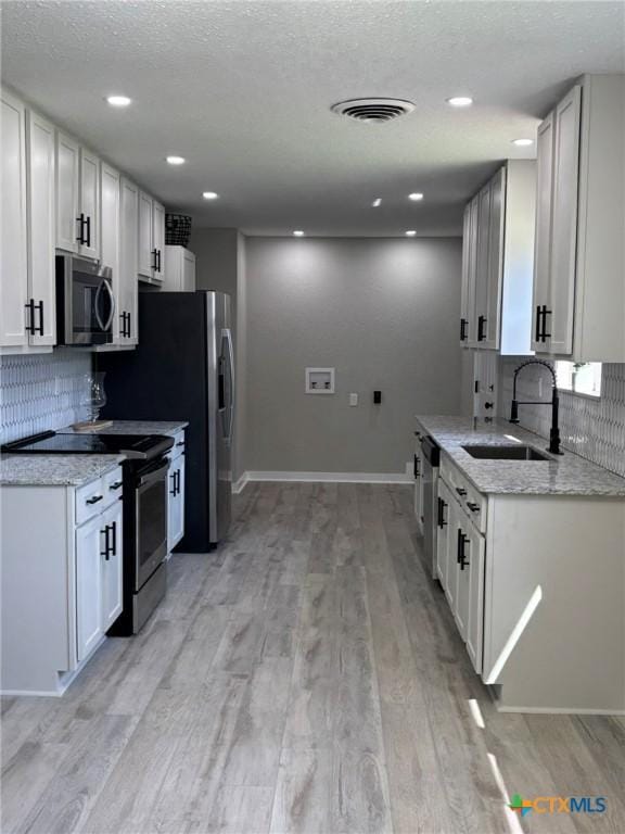 kitchen featuring sink, white cabinets, stainless steel appliances, light stone countertops, and light hardwood / wood-style flooring