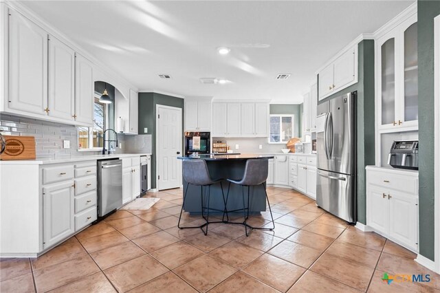 kitchen featuring a breakfast bar area, light tile patterned floors, a kitchen island, white cabinets, and appliances with stainless steel finishes