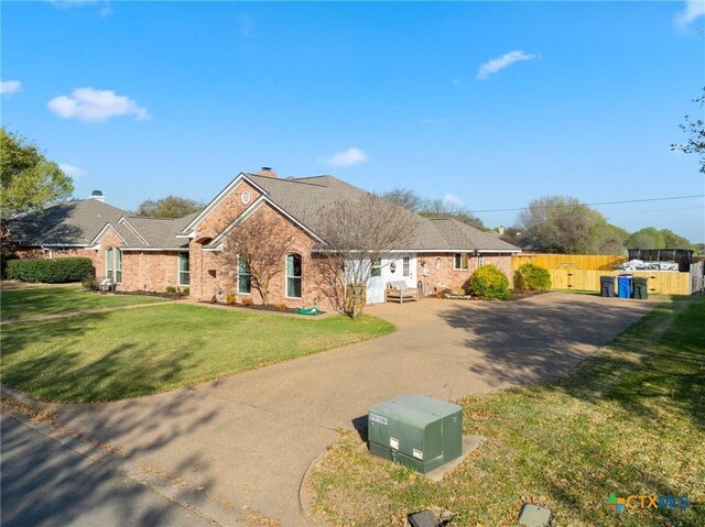 single story home featuring a front yard, fence, brick siding, and concrete driveway