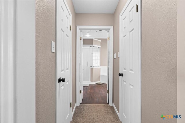 corridor with baseboards, carpet floors, and a textured wall