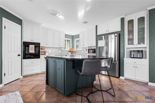 kitchen with a center island, dark countertops, visible vents, white cabinets, and appliances with stainless steel finishes
