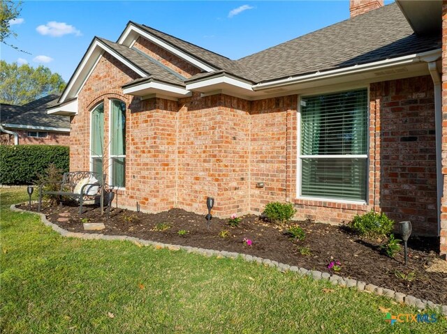 view of property exterior with a lawn, a chimney, brick siding, and roof with shingles