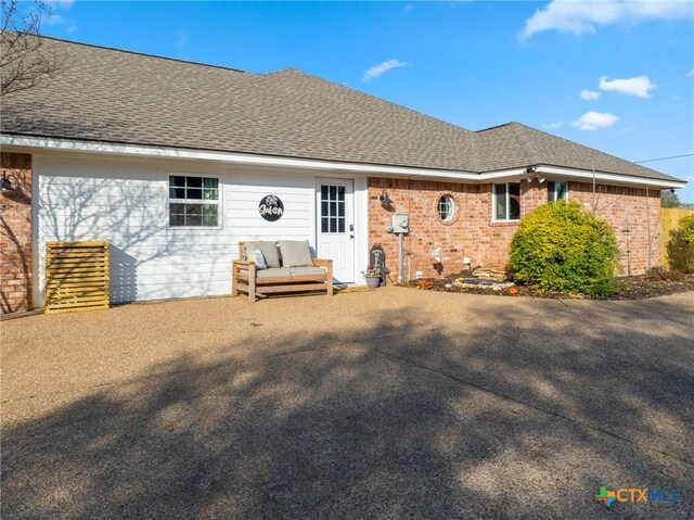 rear view of house featuring brick siding, roof with shingles, and a patio area