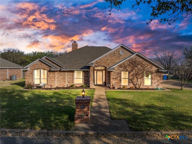 ranch-style house with central air condition unit, a chimney, a front yard, and brick siding