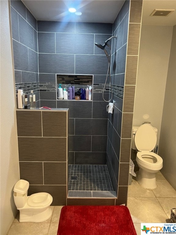 bathroom featuring toilet, tile patterned flooring, and tiled shower