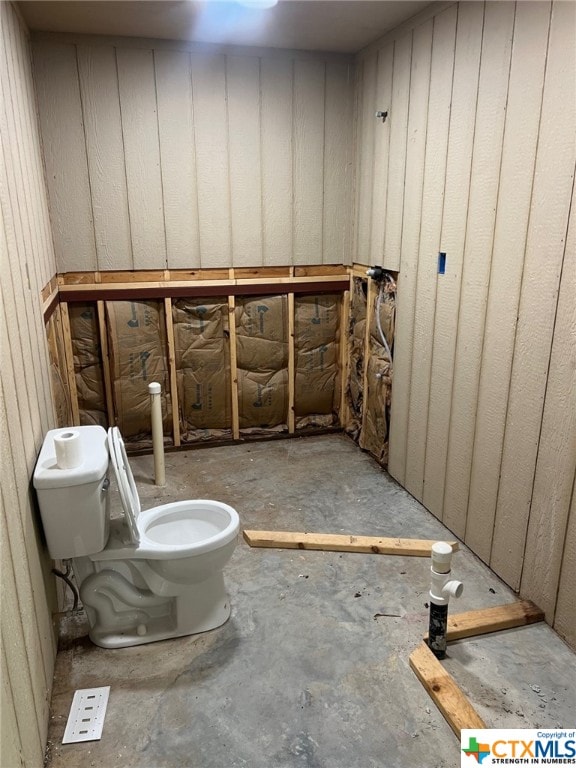 bathroom with wood walls, concrete floors, and toilet